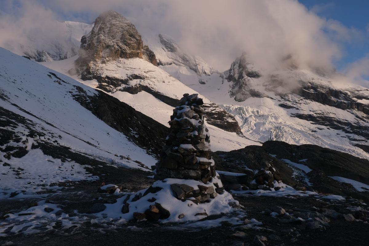 A tall cairn backed by snow covered mountains at the top of The Hohtürli Pass (2778m), Switzerland