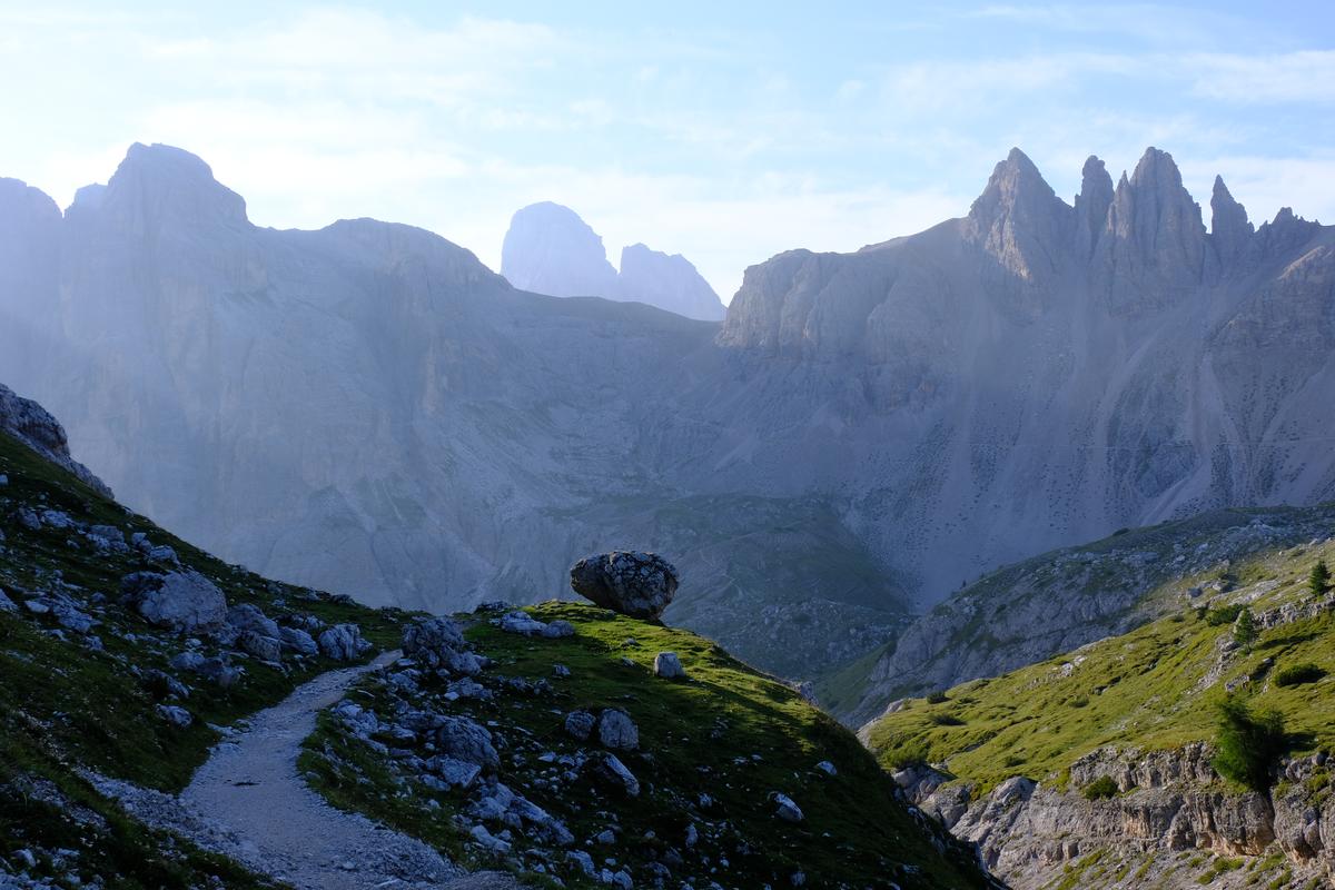A large boulder perched on the edge of a cliff with the Dolomites receding in the background. Italy