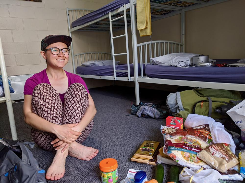 Rose sits on the floor of our hostel dorm room, some of our grocery shopping is visible beside her.
